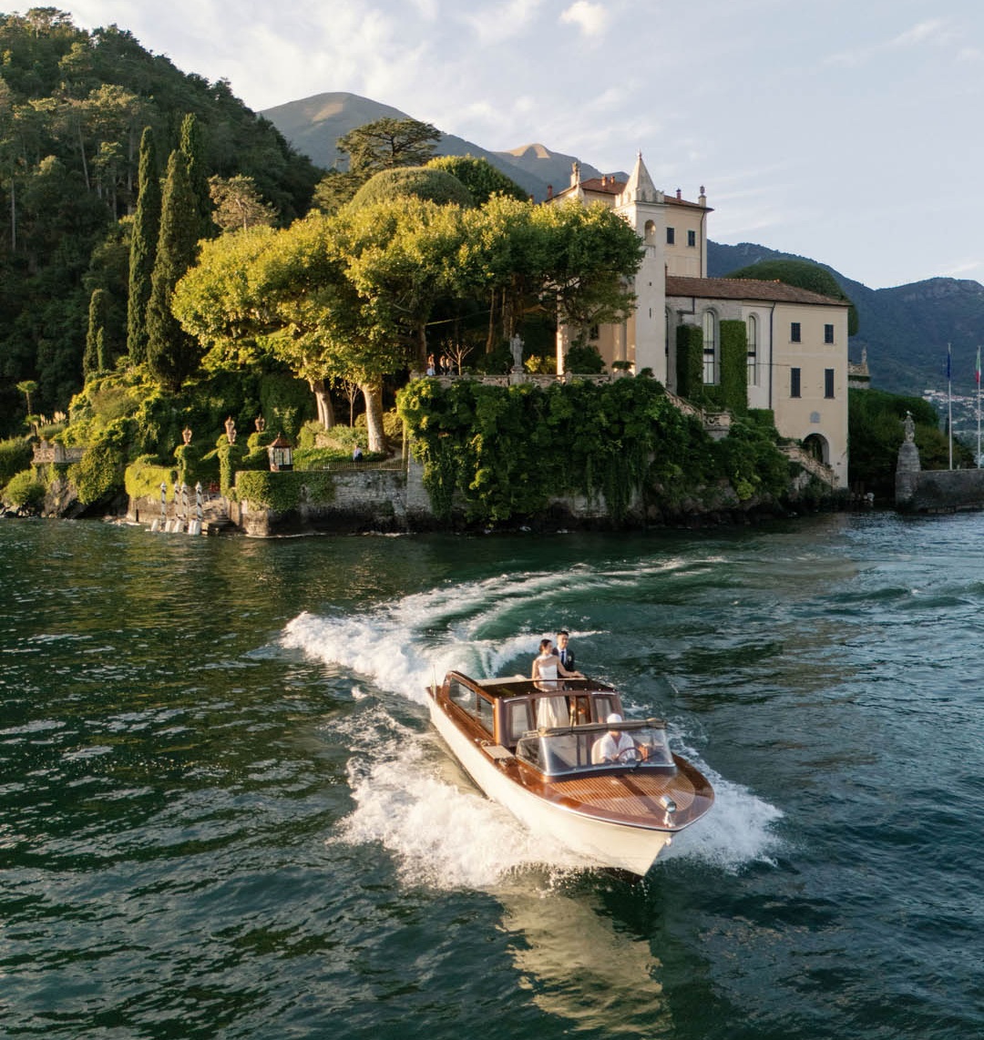 Taxi veneziano in legno con sposi e capitano sul lago di Como davanti a Villa del Balbianello e ai suoi giardini